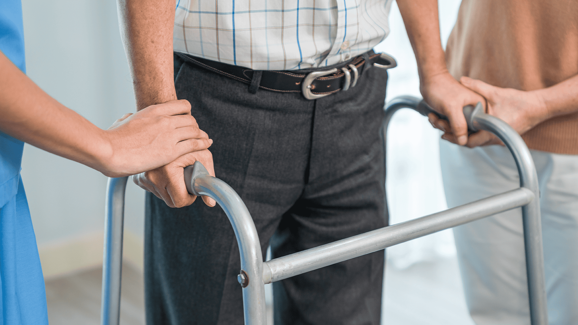 Чоловік тримається за ходунки, його підтримують жінки по обидва боки.