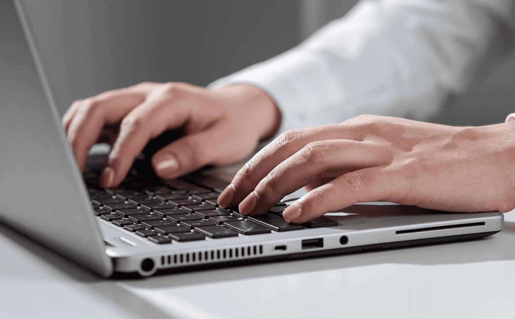 Людина працює за сірим ноутбуком. Руки знаходяться на клавіатурі.